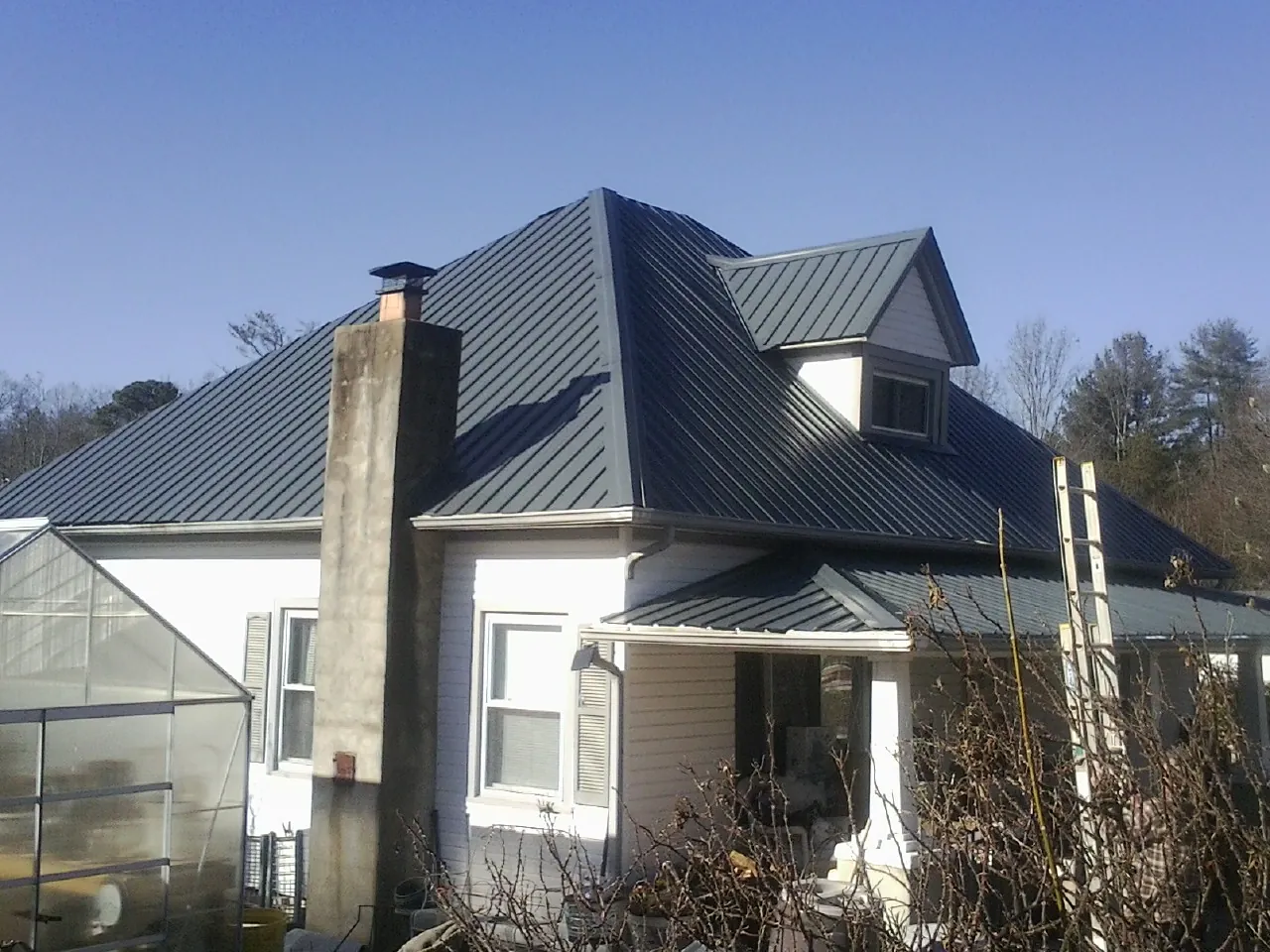 Dark blue standing seam metal roof on a white farmhouse with dormer — Slate & Tile Roof Repair by Roofing Brothers in Vian
