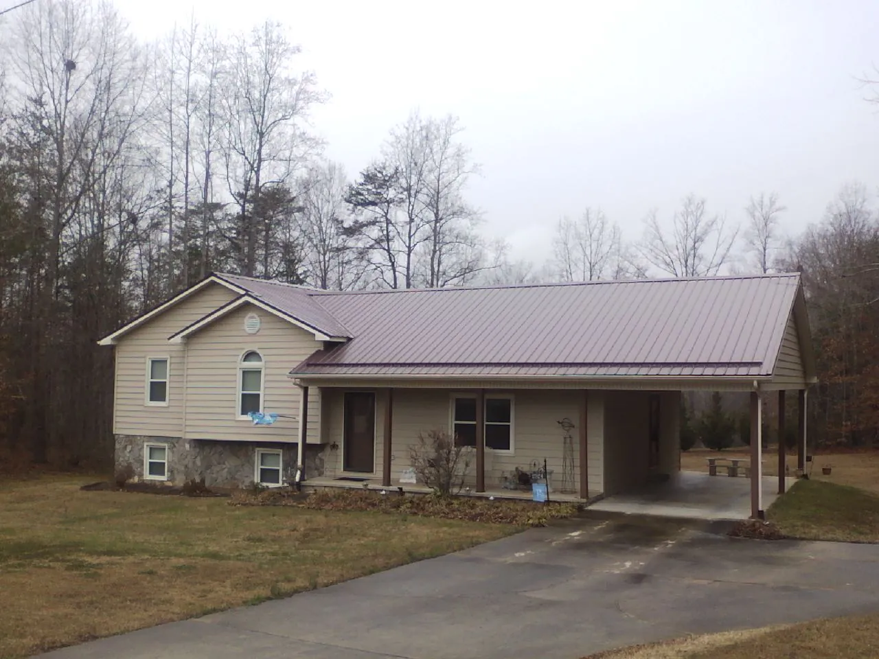 Burgundy metal roof on a tan split level home with an attached carport in Vian