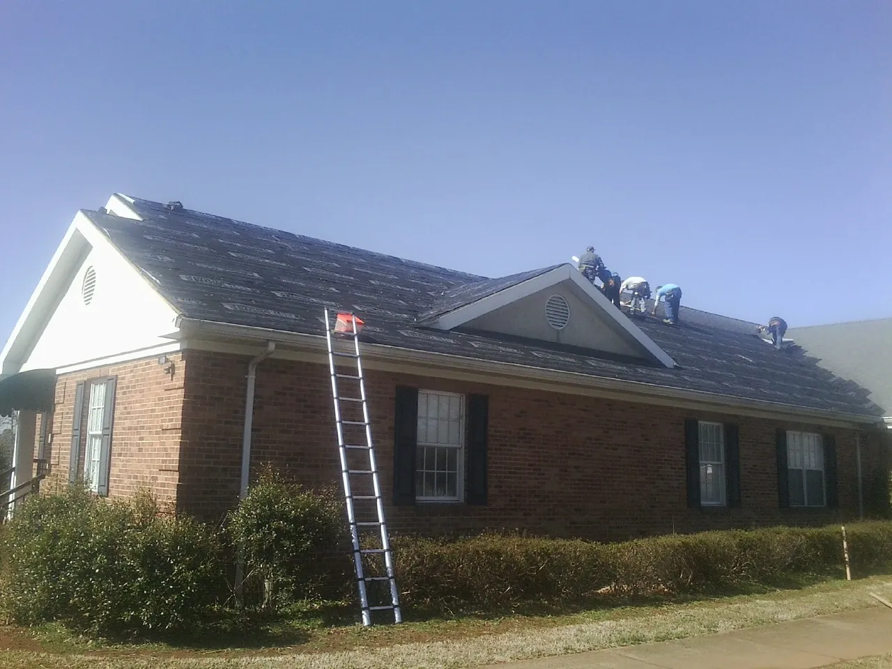 Crew tearing shingles off a brick ranch roof with a ladder set — Emergency Roof Repair work by our crew in Vian