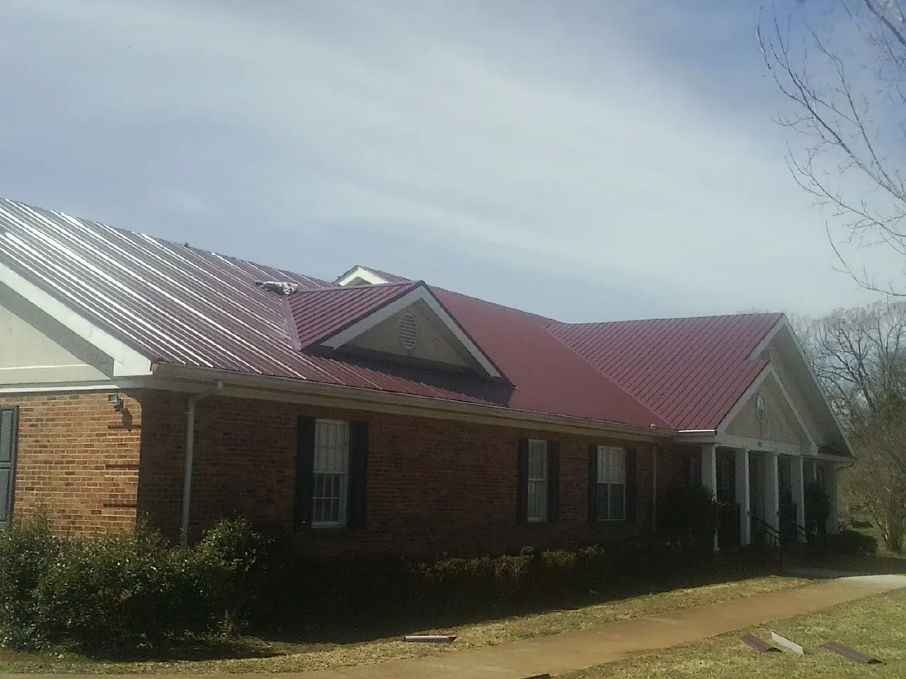 Red metal roof with gabled entries on a long brick building, from a Hail Damage Roof Repair job in Vian
