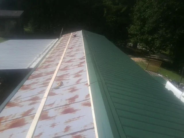 Old rusted panels beside newly installed green metal roofing — Wind Damage Roof Repair by Roofing Brothers in Vian