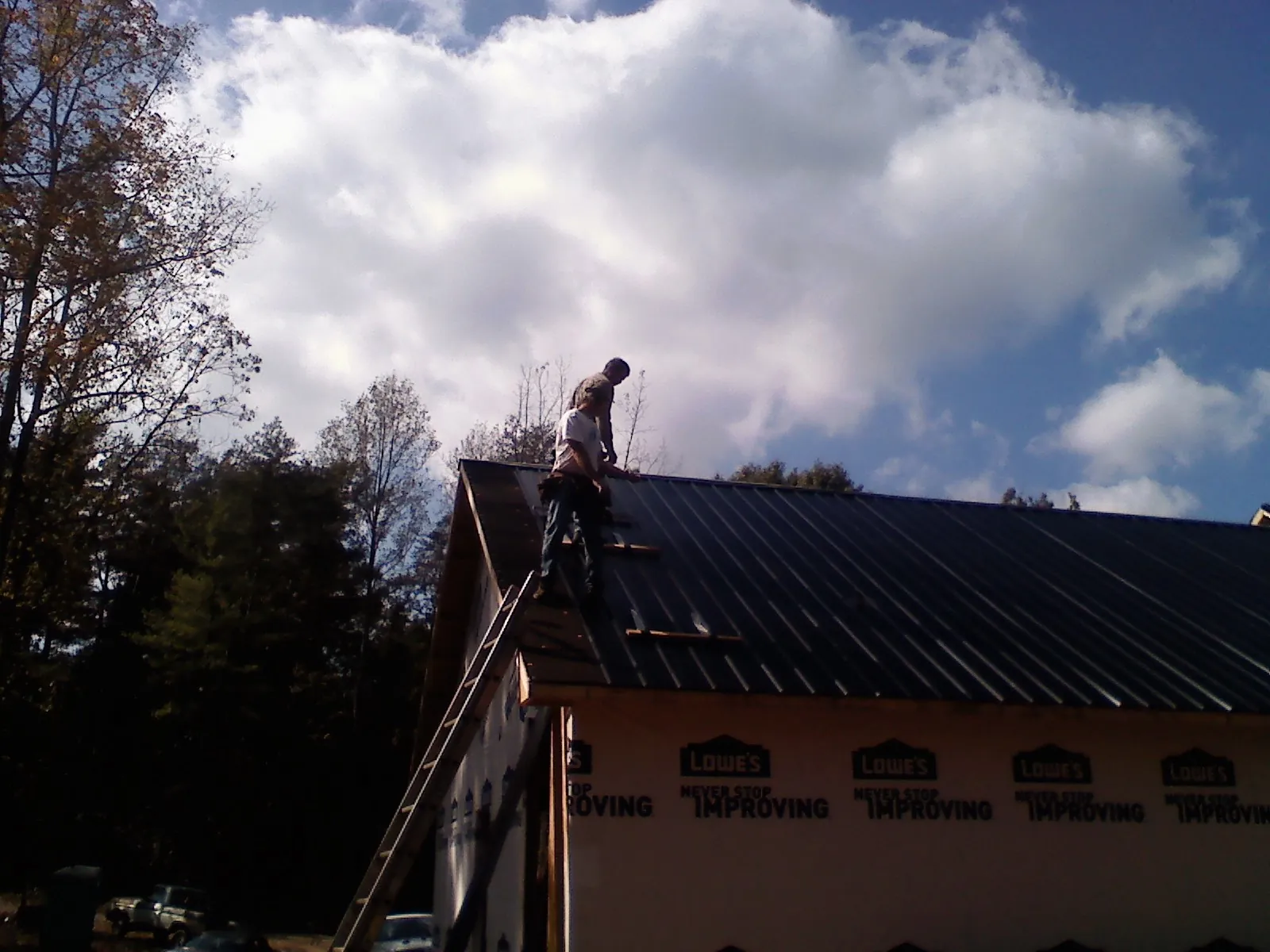 Roofer fastening dark metal panels high against a cloudy sky, from a Roof Inspection job in Vian