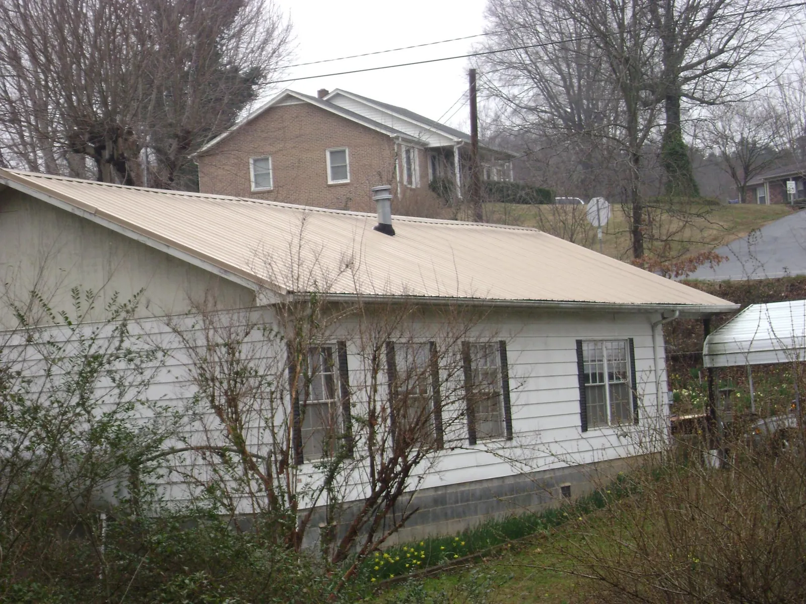 Tan metal roof on a white sided house set into a hillside — Commercial Roofing by Roofing Brothers in Vian
